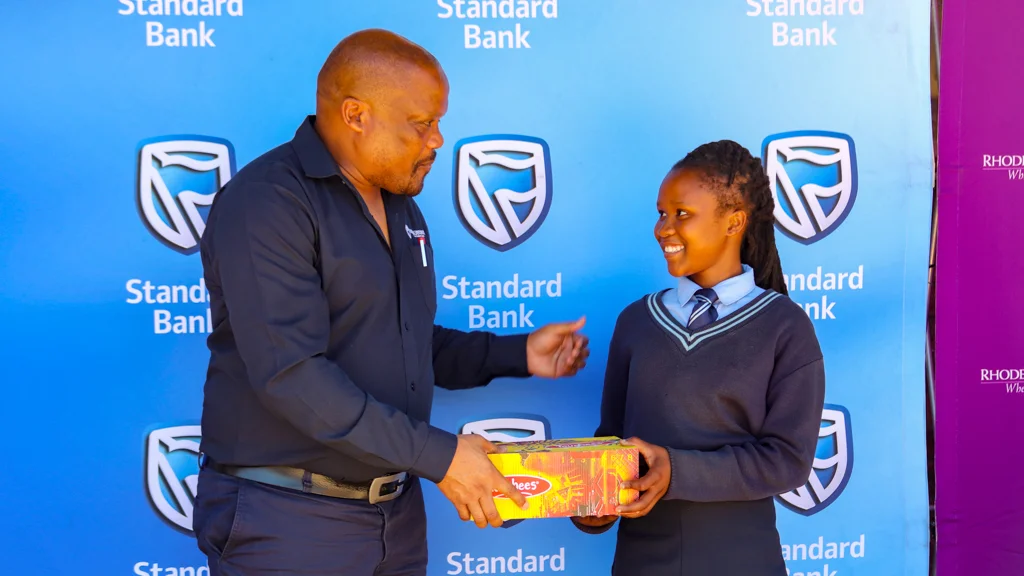Communications and Advancement Director, Dr Luzuko Jacobs hands over a box of new shoes to grade 9 learner, Aviwe Fanki. Picture credit: Vusumzi Fraser Tshekema. 