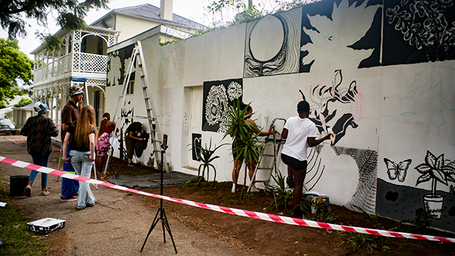 First-year Fine Art mural in progress on Somerset Street. With Dr Jeannine-Madeleine Fischer and Mook Lion pictured to the left. [CREDIT: Sam van Heerden]