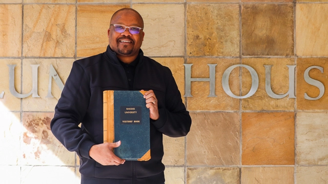 Director of Communication and Advancement, Luzuko Jacobs, with the Visitors' Book outside the Alumni House building
